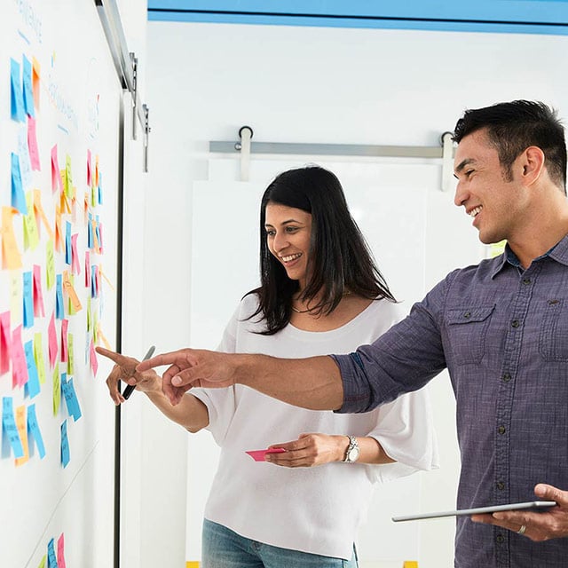 Man and woman in front of whiteboard with sticky notes of innovative ideas.